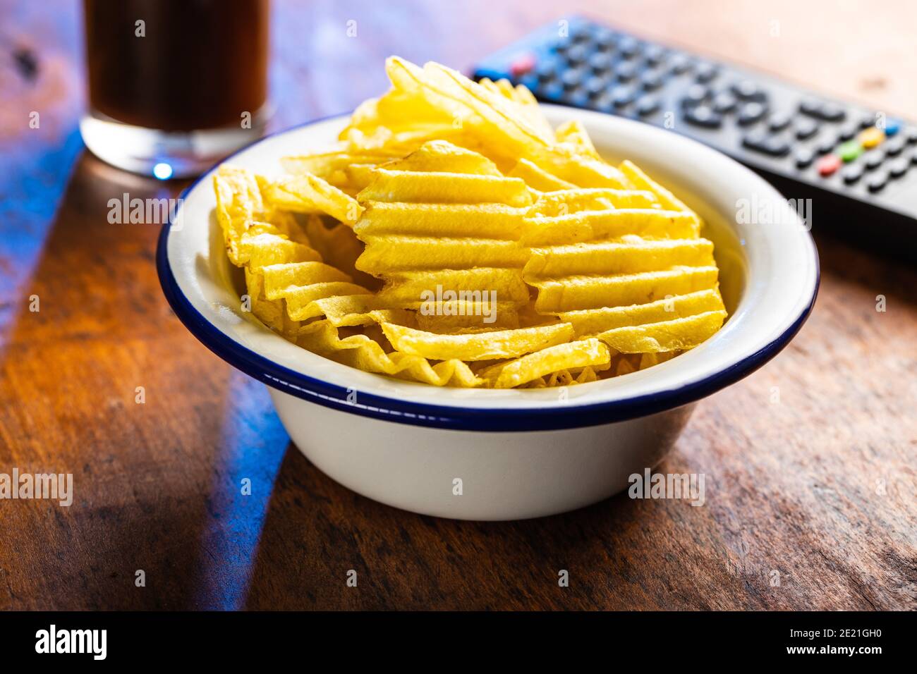 Crispy potato chips in bowl on wooden table Stock Photo