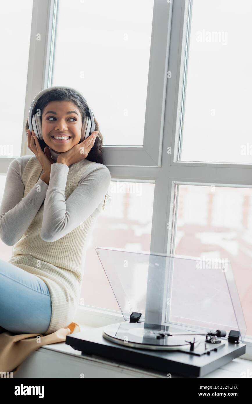 cheerful african american woman touching wireless headphones while ...