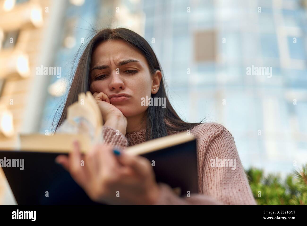 Upset and distressed female brunette is reading book in city street Stock Photo