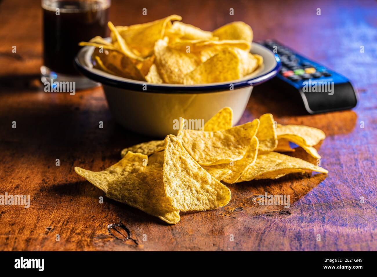 Salted tortilla chips. Yellow nachos triangle and tv remote control on wooden table. Stock Photo