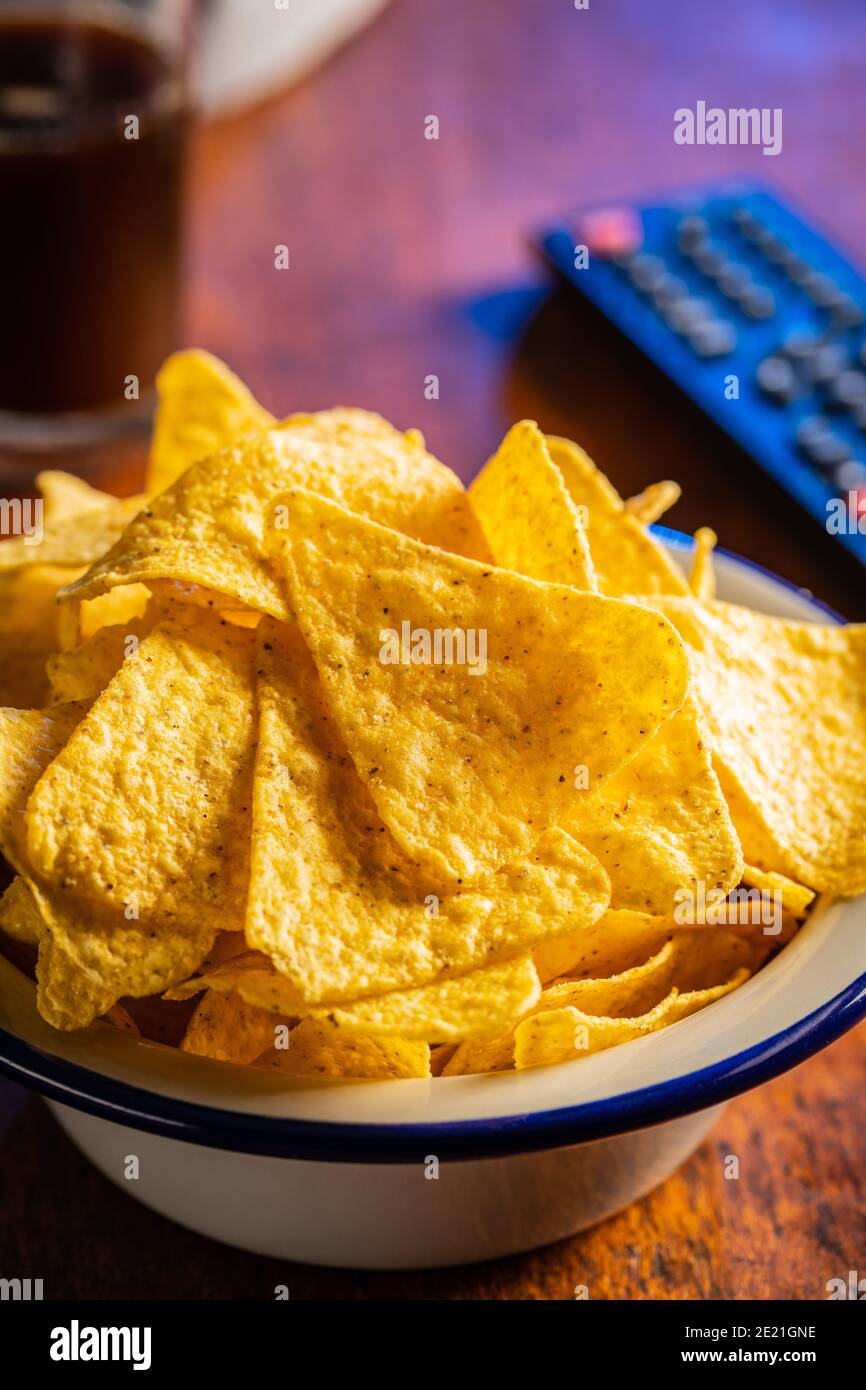 Salted tortilla chips. Yellow nachos triangle and tv remote control on wooden table. Stock Photo