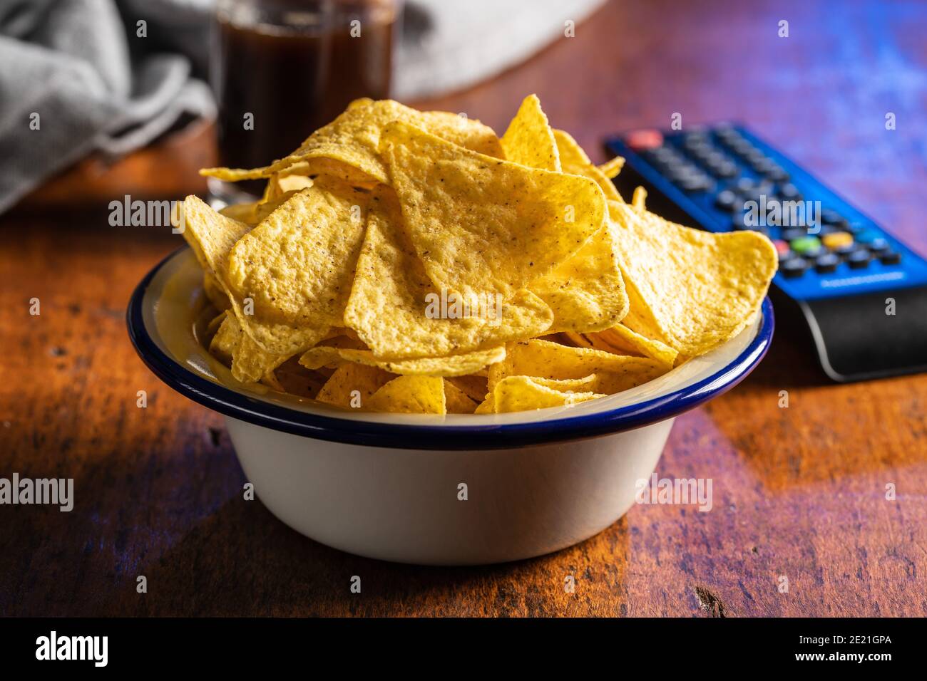 Salted tortilla chips. Yellow nachos triangle and tv remote control on wooden table. Stock Photo