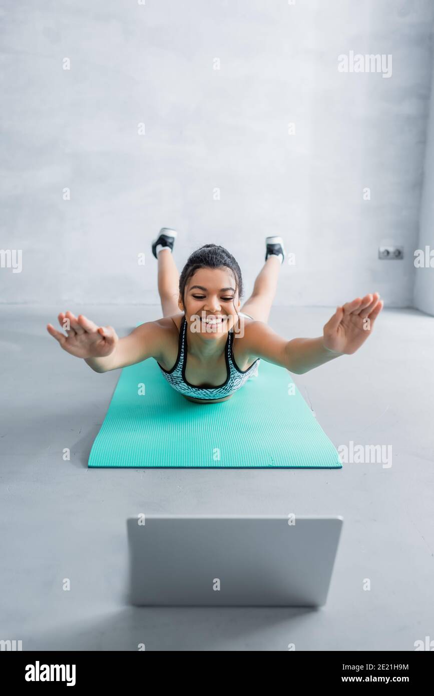 cheerful african american sportswoman in locust pose near laptop on blurred foreground Stock Photo