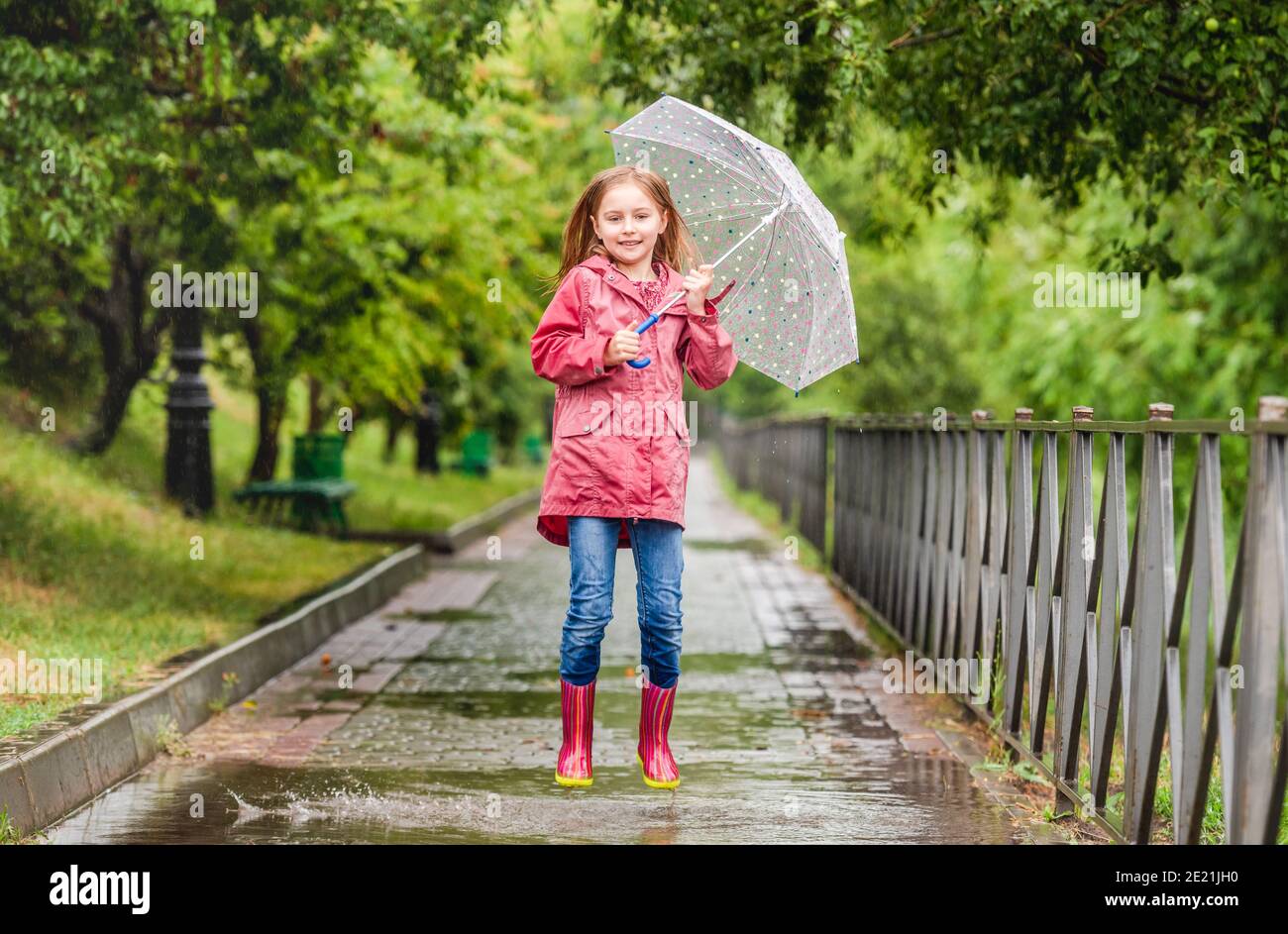 Little girl with umbrella jumping in puddle during rainy walk in park ...