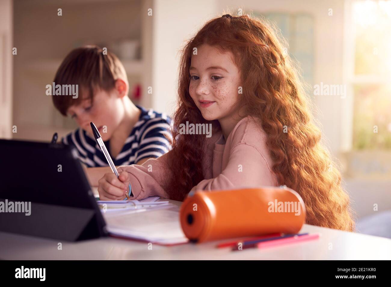 Two Children Sitting At Kitchen Counter Doing Homework Using Digital Tablet Stock Photo