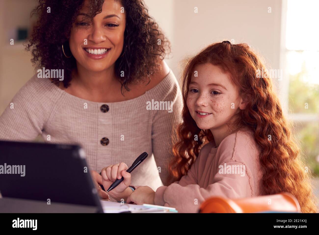 Mother Helping Daughter With Homework Sitting At Kitchen Counter Using ...