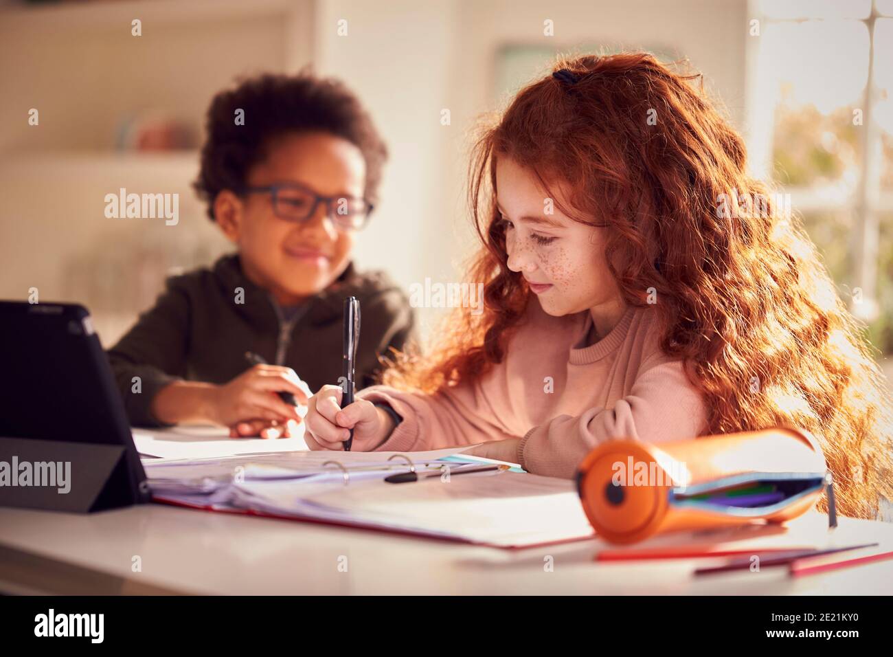Two Children Sitting At Kitchen Counter Doing Homework Using Digital Tablet Stock Photo