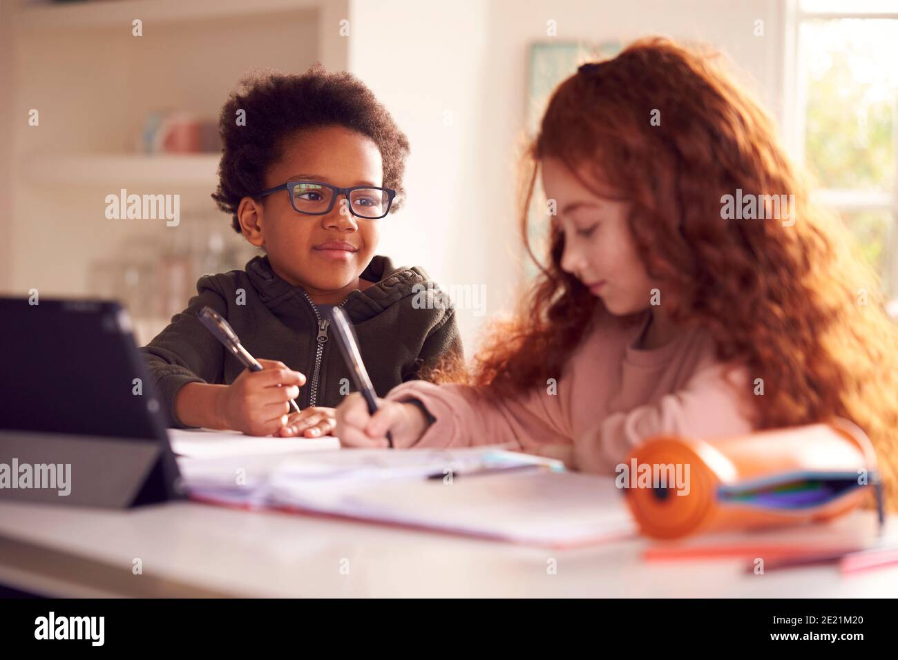 Two Children Sitting At Kitchen Counter Doing Homework Using Digital Tablet Stock Photo