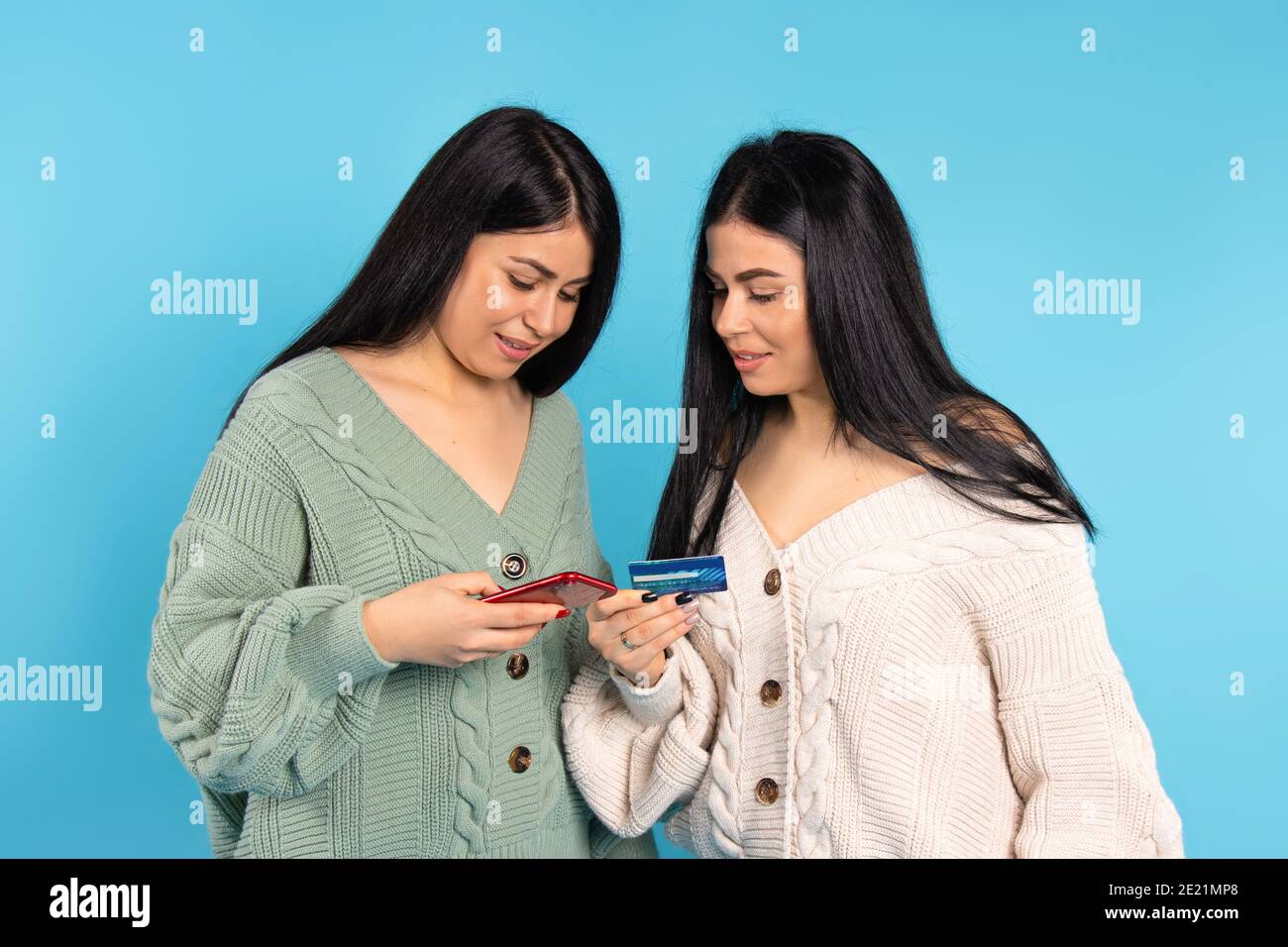 Twins Using A Mobile Phone To Make An Online Payment With A Bank Card Blue Background Stock Photo Alamy