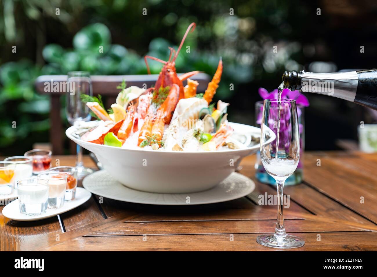 Waiter pouring white wine into wine glass and serving to customer in restaurant with big bowl seafood on ice in background. Restaurant gastronomy food Stock Photo