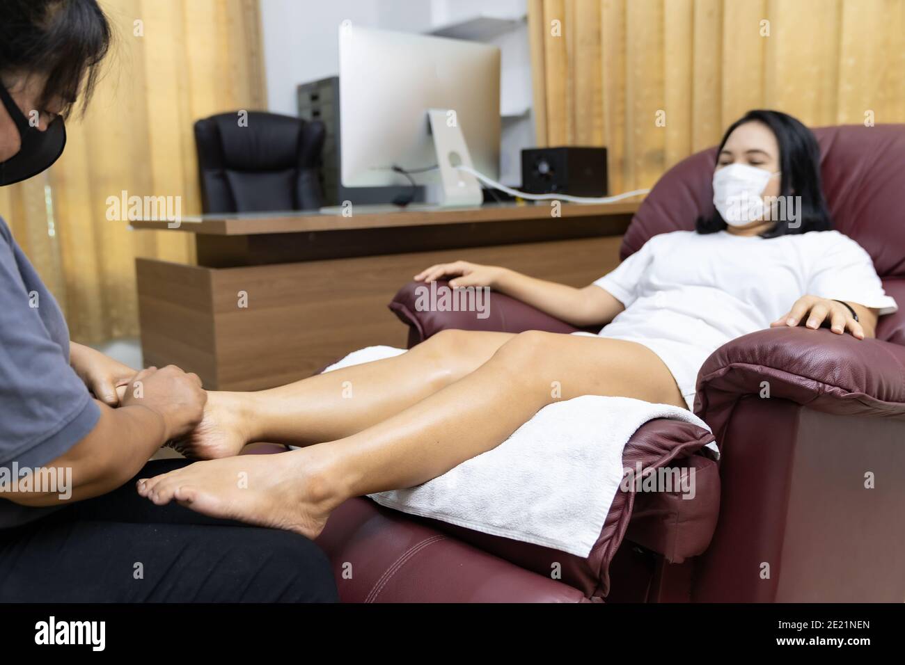 Quarantine asian woman do foot massage at home with face mask while city lockdown for social distance due to coronavirus pandemic. Massage is one of s Stock Photo