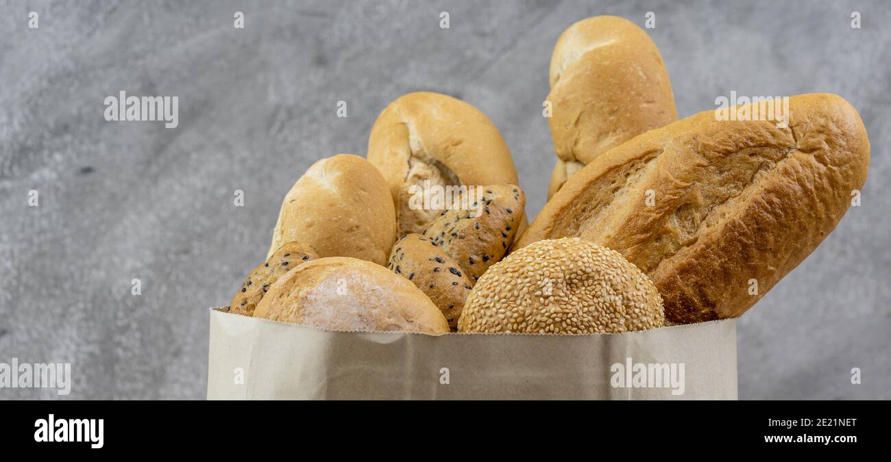 Variety bread in disposable paper bag on grey vintage loft background. Bakery food and drink and grocery concept for delivery. Panoramic web banner cr Stock Photo