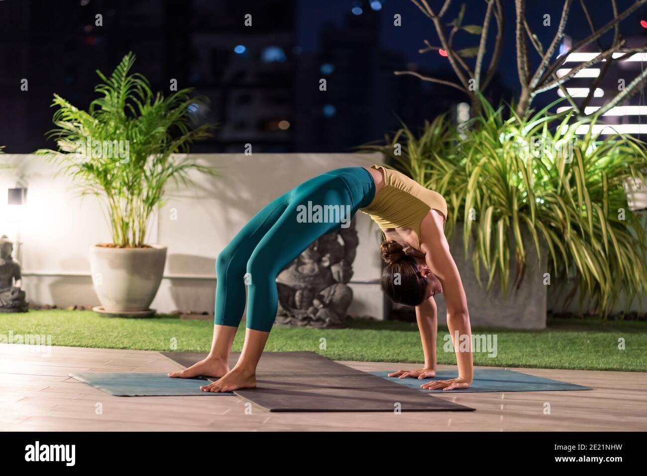 Asian female woman in sportswear bra pants practicing yoga during city lockdown alone in her apratment with background of cityscape illumination at ni Stock Photo