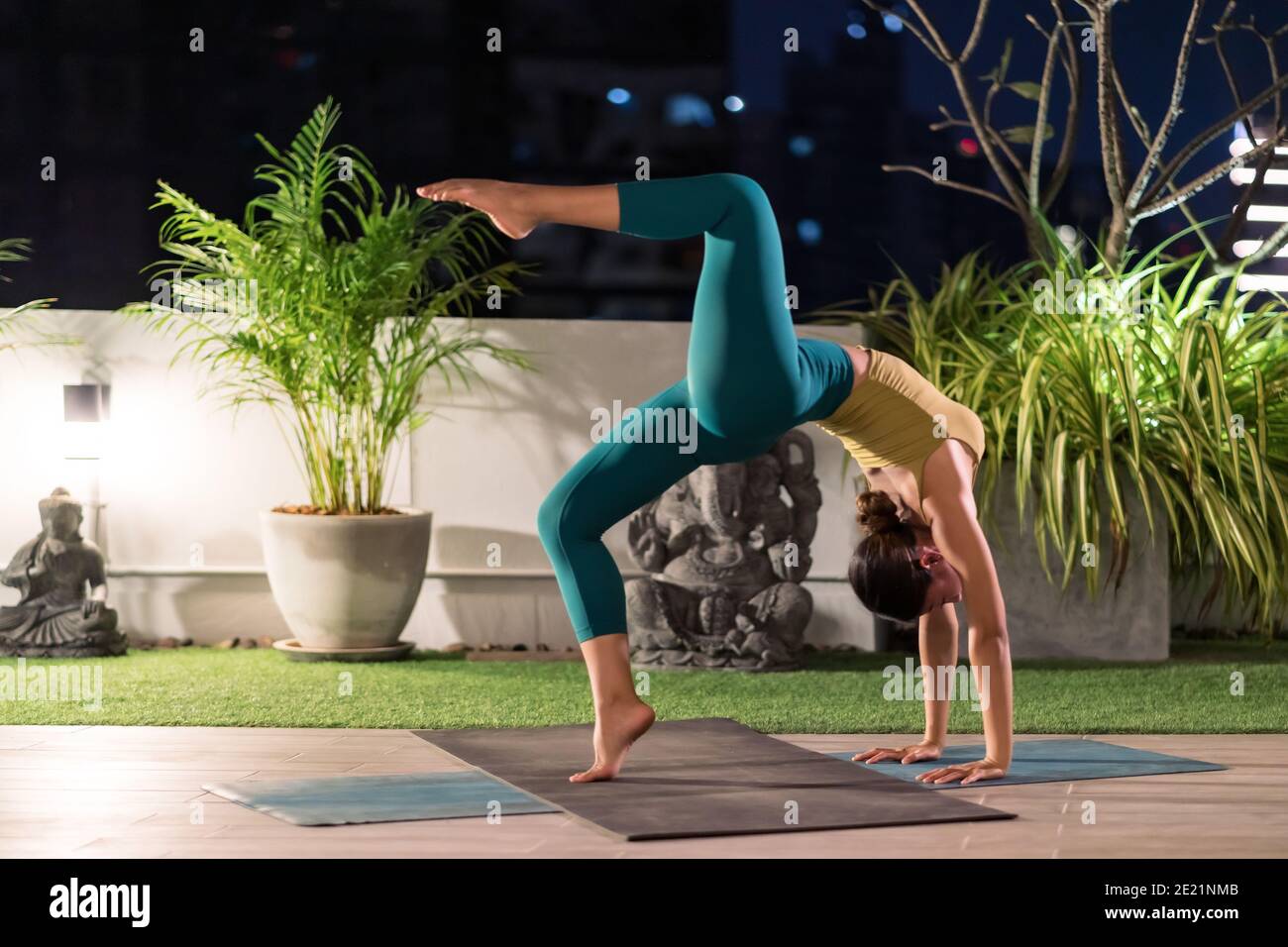 Asian female woman in sportswear bra pants practicing yoga during city lockdown alone in her apratment with background of cityscape illumination at ni Stock Photo