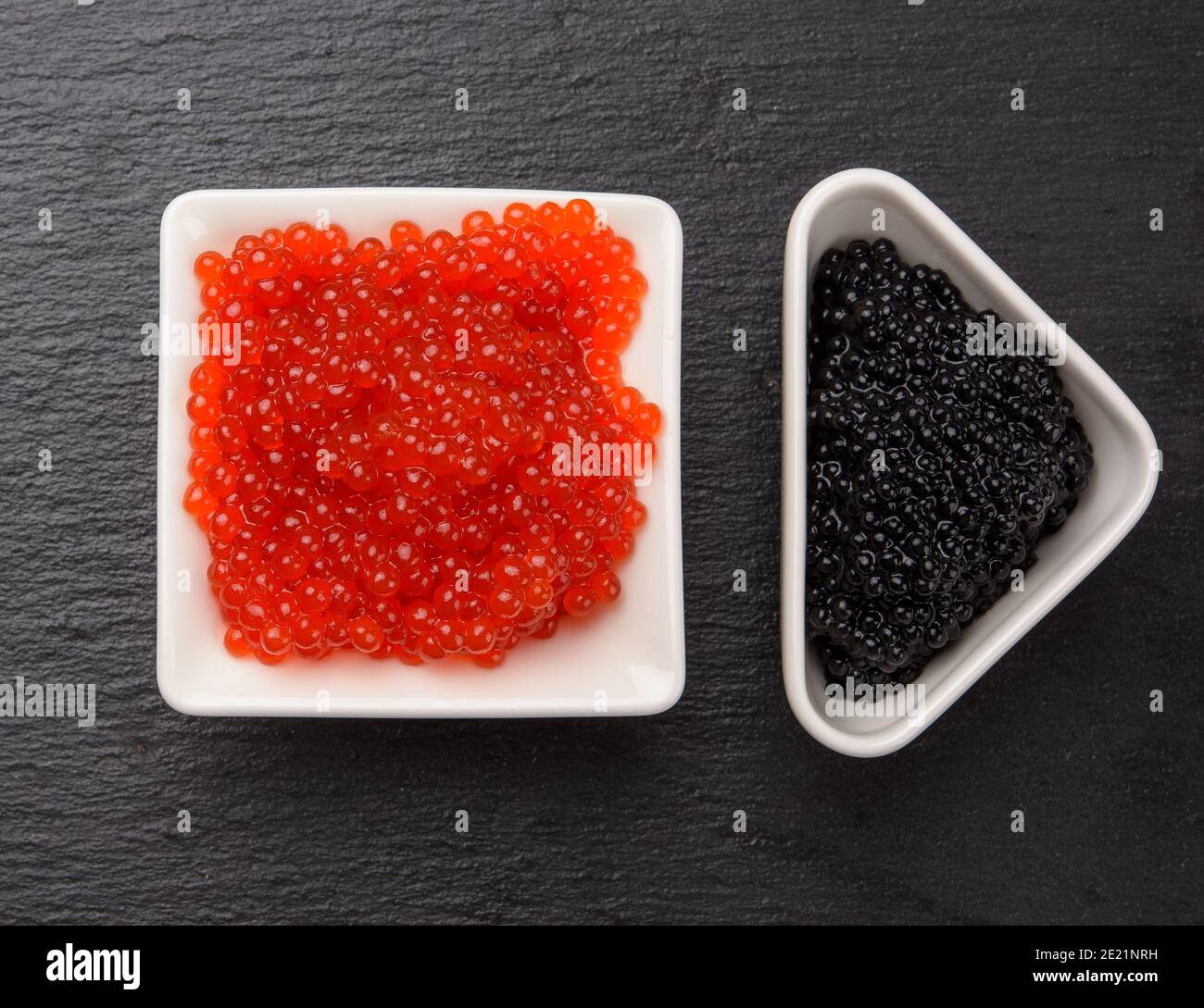 grainy caviar of paddlefish fish in a white ceramic plate and red chum salmon caviar in a white ceramic bowl, black background, top view Stock Photo