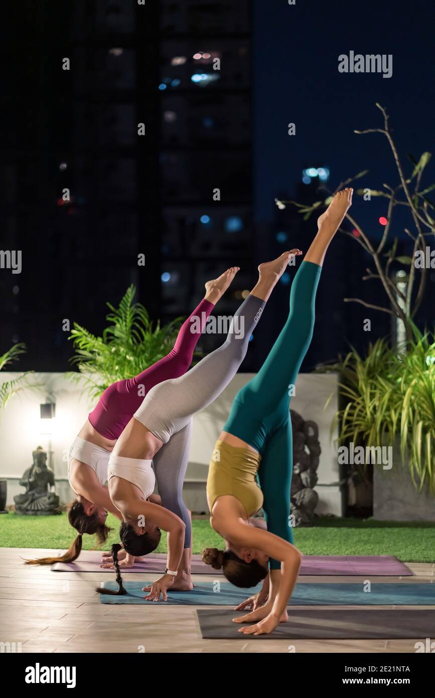 Group of asian women in sportswear pants practicing yoga during city lockdown in their apratment with distance in background of cityscape illumination Stock Photo