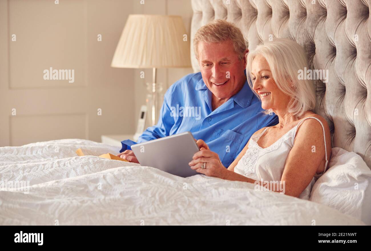 Senior Couple At Home In Bed Self Isolating Using Digital Tablet During Covid 19 Lockdown Stock Photo