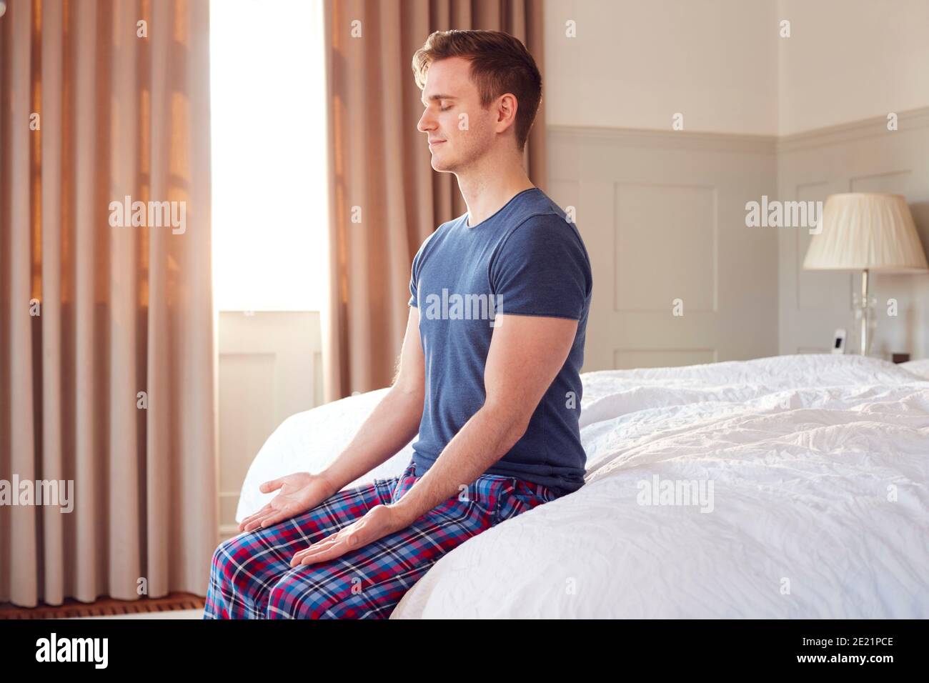 Man Sitting On Edge Of Bed At Home Meditating During Lockdown For Covid-19 Stock Photo