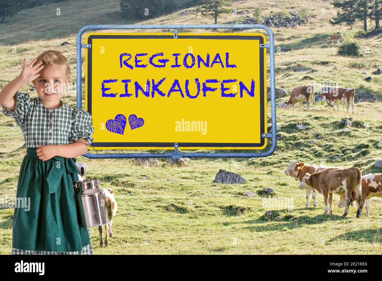 A small child in a dirndl with a milk jug in her hand in front of an alpine meadow with cows and the sign 'Buy regional'.Lettering German language Stock Photo
