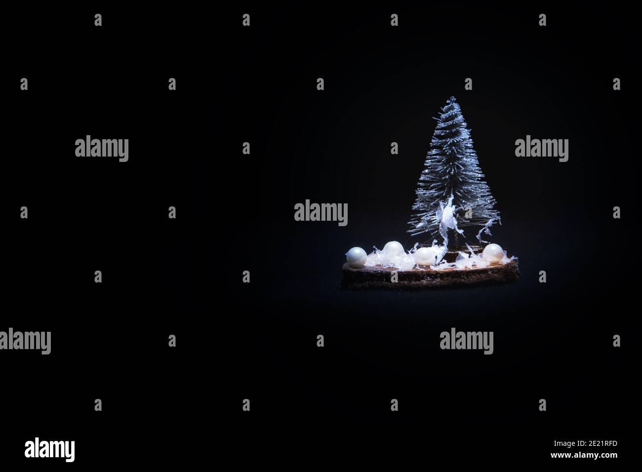 Christmas decoration, snowy fir tree with beads on wooden plate on black with text space . Stock Photo