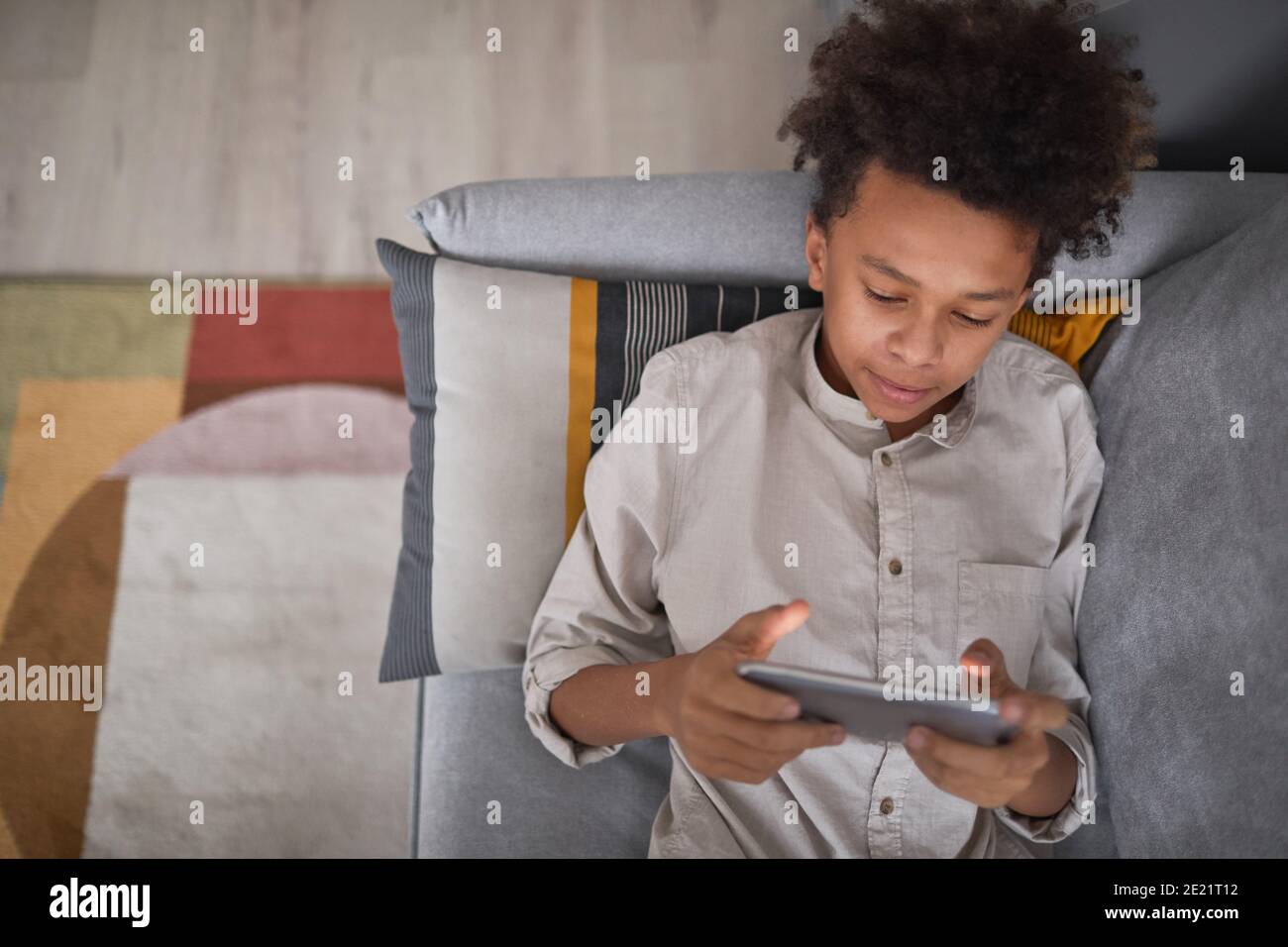 From above view medium portrait of teen boy relaxing on sofa at home playing video game on smartphone, copy space Stock Photo