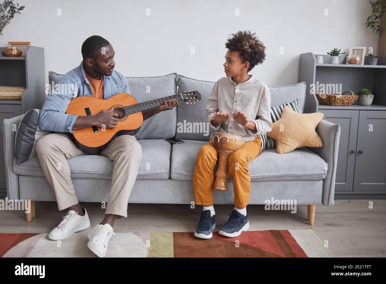 Horizontal full shot of African American man and his son spending time together at home playing guitar and djembe Stock Photo