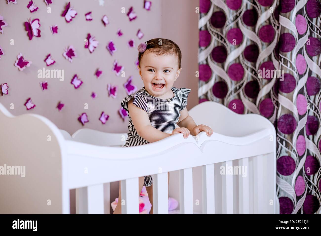 Cute, adorable baby enjoying her childhood in her crib. Nice deocrated bedroom with lots of butterflies Stock Photo