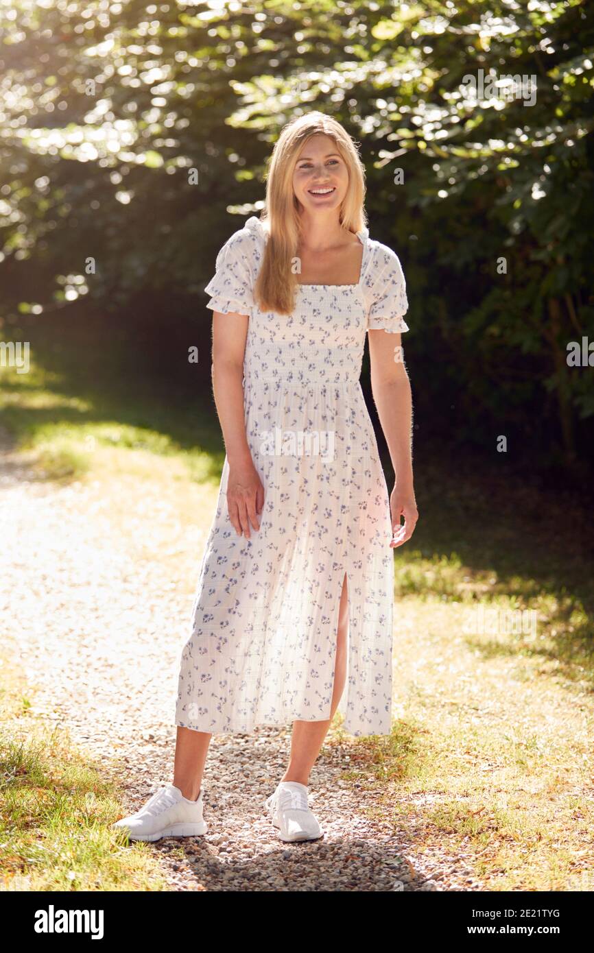 Full Length Portrait Of Smiling Woman Wearing Summer Dress Walking Along Countryside Path Stock Photo