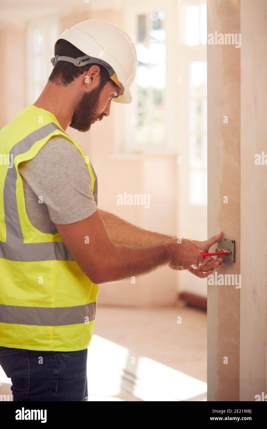 Electrician Wearing Hard Hat Fitting Light Switch At New Build Property
