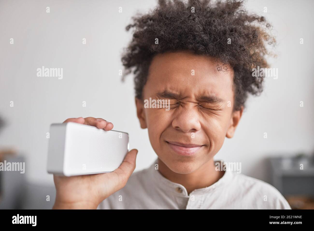 Close-up portrait of stylish African American kid holding wireless smart speaker enjoying favorite music with eyes closed Stock Photo