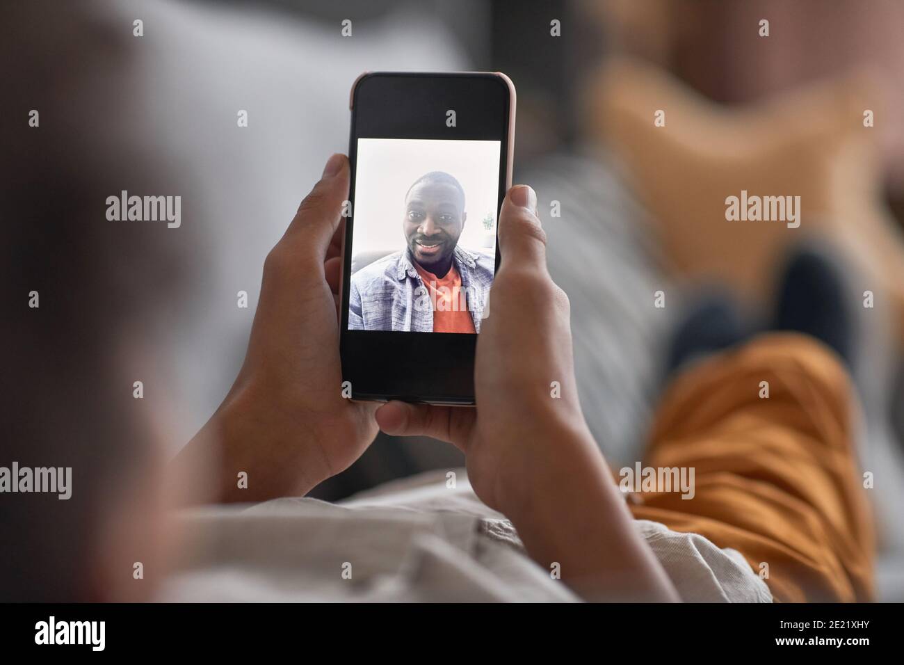 Unrecognizable child relaxing on sofa holding smartphone in his hands having online call with his father Stock Photo