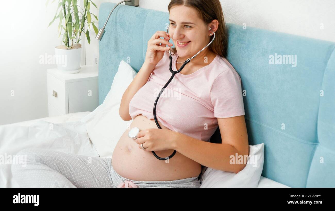 Happy smiling pregnant woman using stethoscope to listen her baby