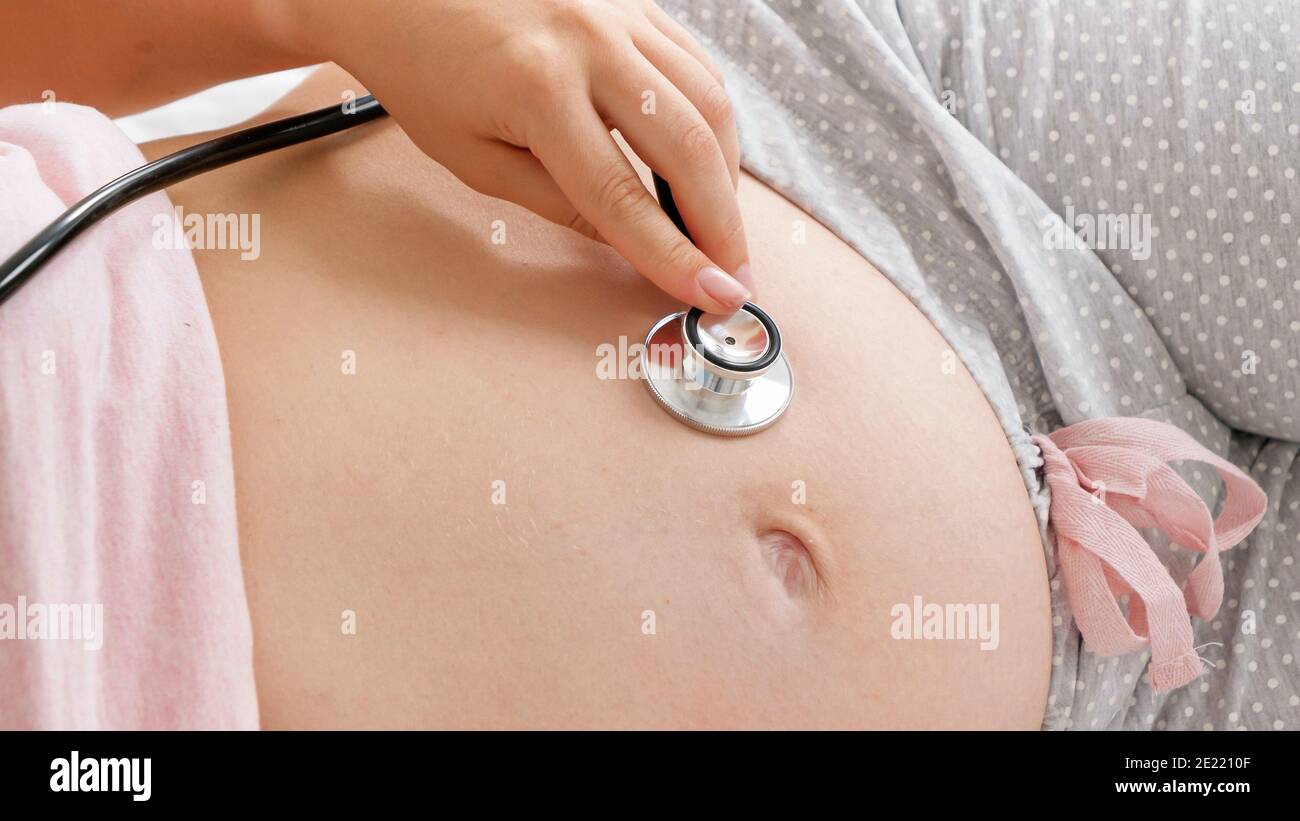 woman pregnant pink bra looking down at belly with stethoscope