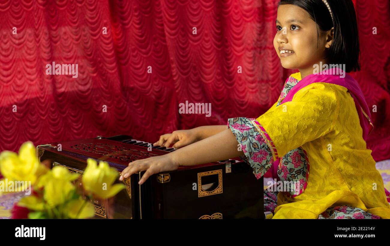 side view of an Indian cute girl child playing harmonium in ethnic dress Stock Photo