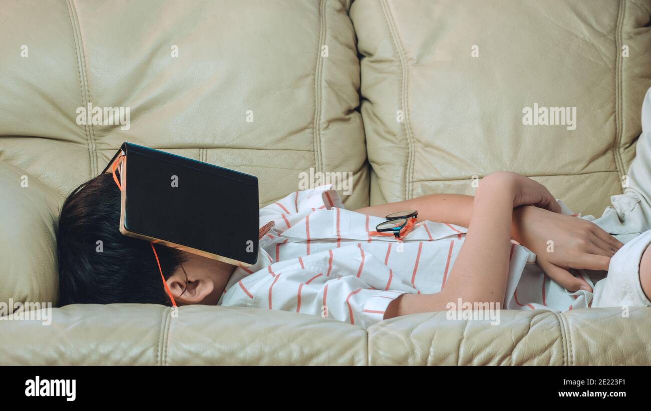Man sleeping on old sofa with book covering his face because reading boook with preparing exam, education concept Stock Photo