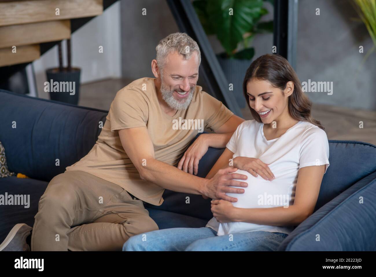 Happy mature man and young pregnant woman sitting and talking Stock