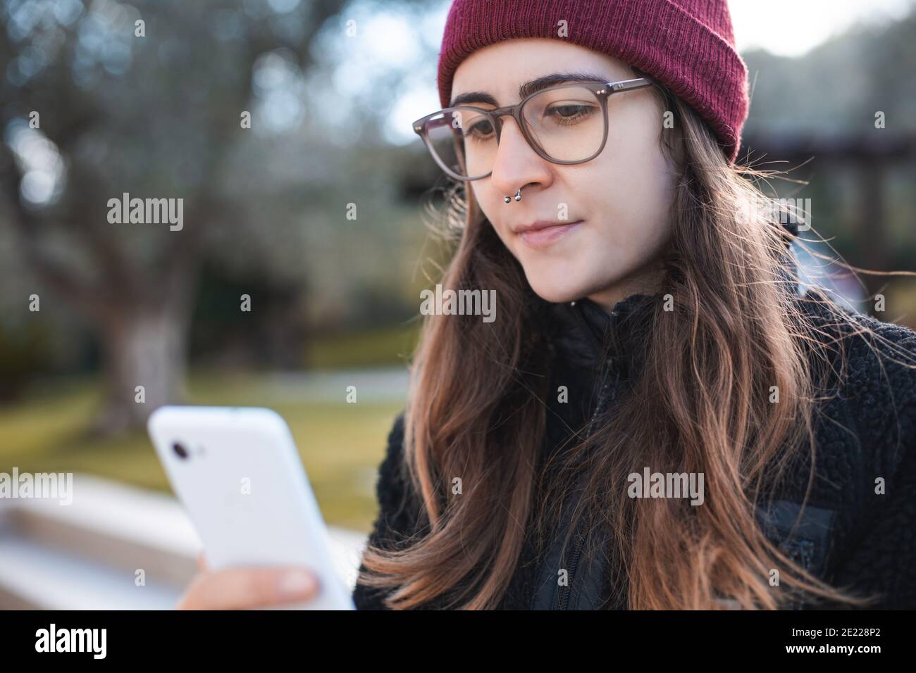 Woman wearing red beanie and glasses smiling using a mobile phone
