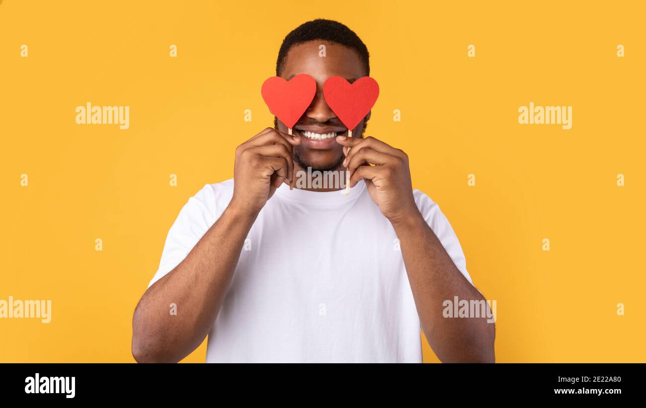 African Guy Covering Eyes With Hearts Over Yellow Studio Background ...
