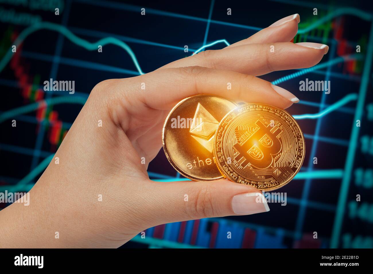 macro female hand holding bitcoin and ethereum side by side in front of stock market chart. Stock Photo