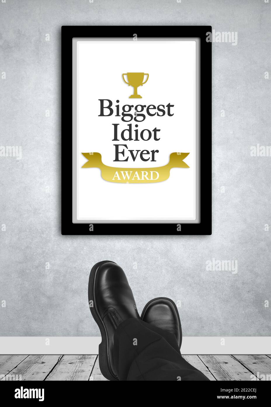 Biggest idiot ever award frame on wall with relaxing business man shoes in foreground Stock Photo
