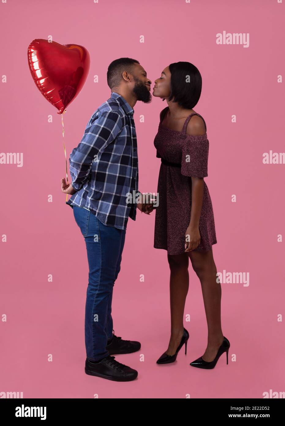 Full length portrait of loving black couple kissing, celebrating Valentine's Day together on pink studio background Stock Photo