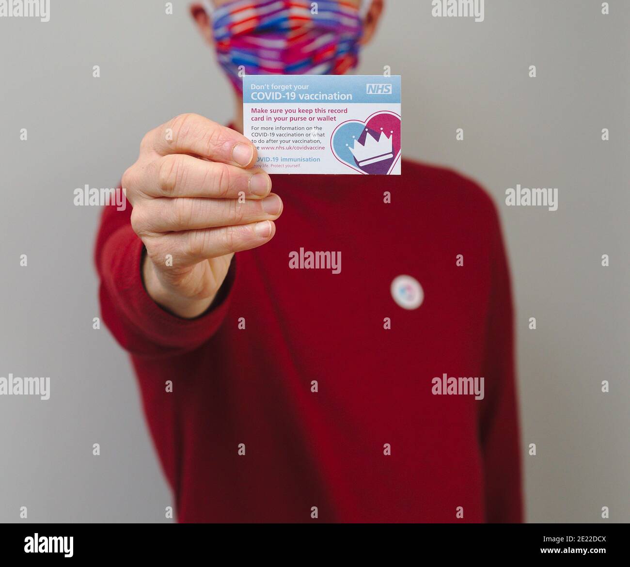 Vaccinated man wearing face mask and holding NHS Covid 19 vaccination record card Stock Photo