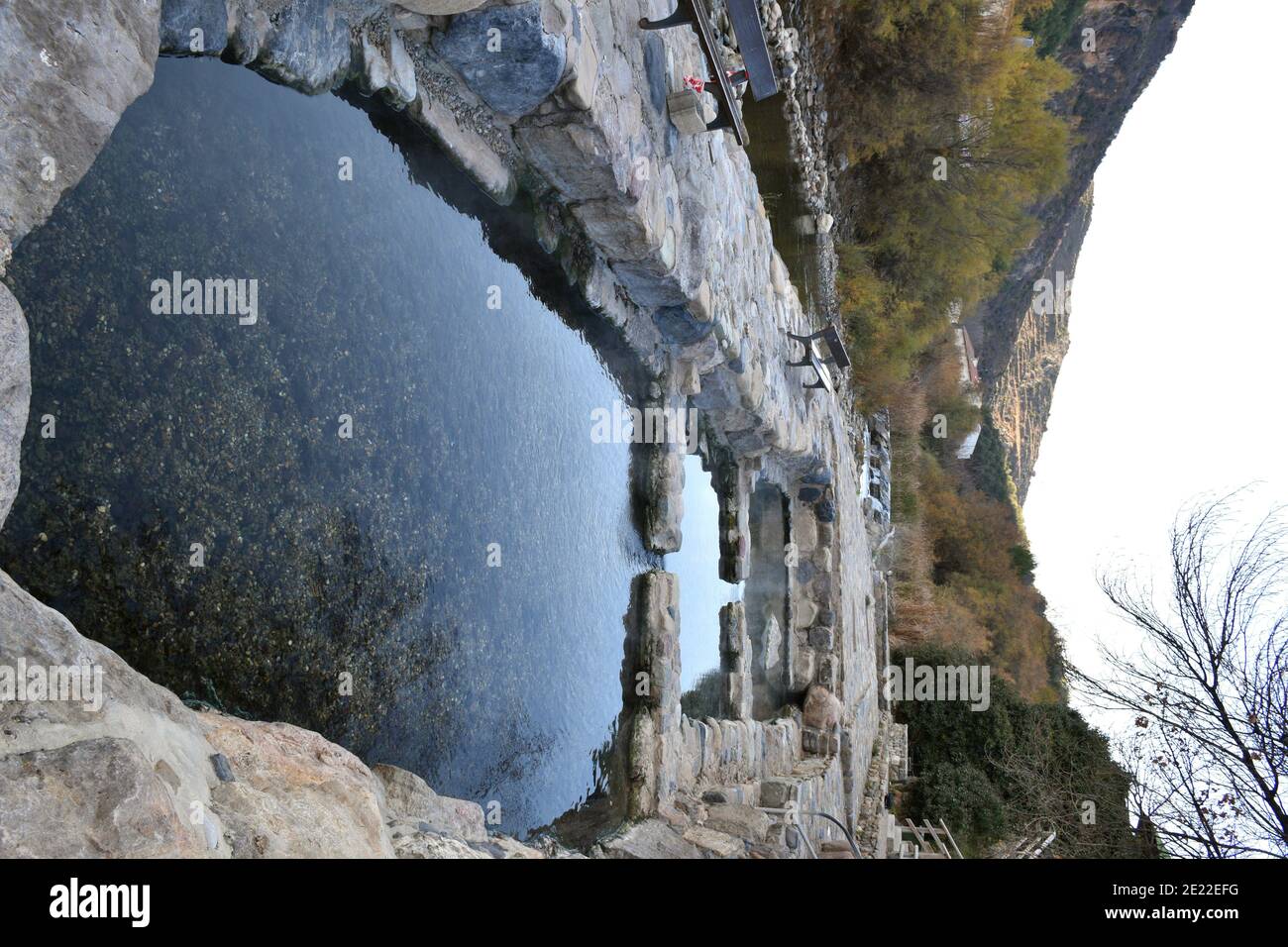 Stone thermal water pools and wooden benches next to the Cidacos river. Hot springs in the village of Arnedillo. Winter day without people. Stock Photo