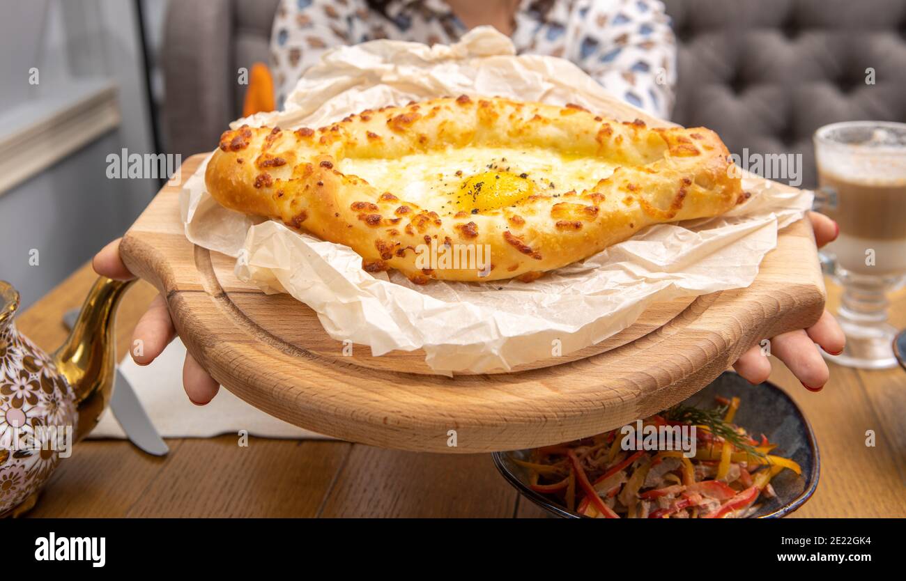 Hands holding khachapuri freshly cooked with egg on wooden tray close up Stock Photo