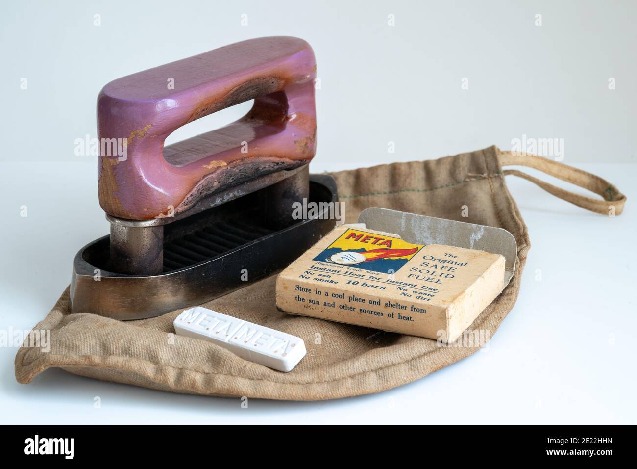 Circa 1930's miniature travel iron with purple handle and a packet of the fuel used to heat it up, Meta Tablets against plain white background. Stock Photo