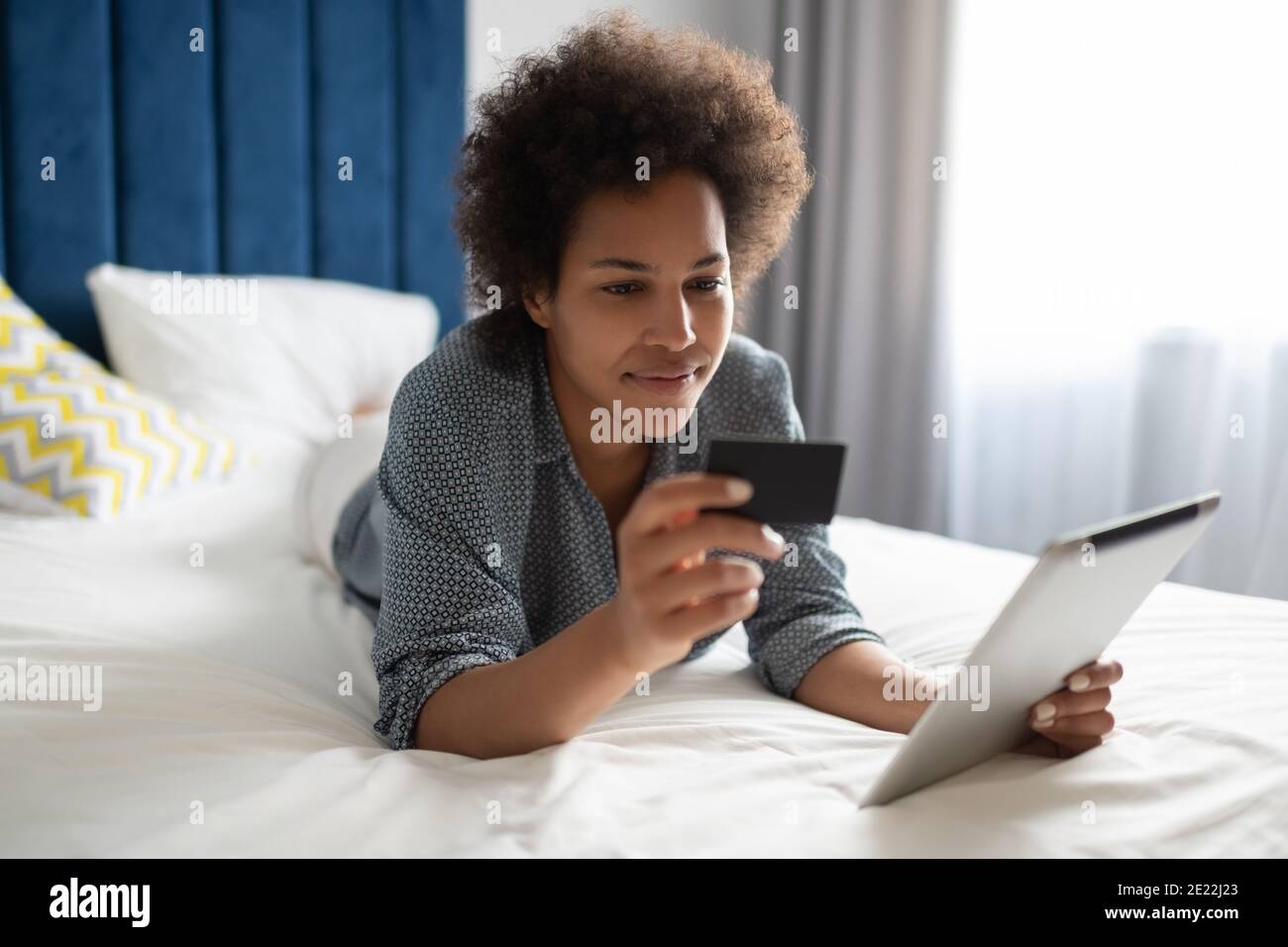 Ethnic female using credit card and tablet for online purchases on bed