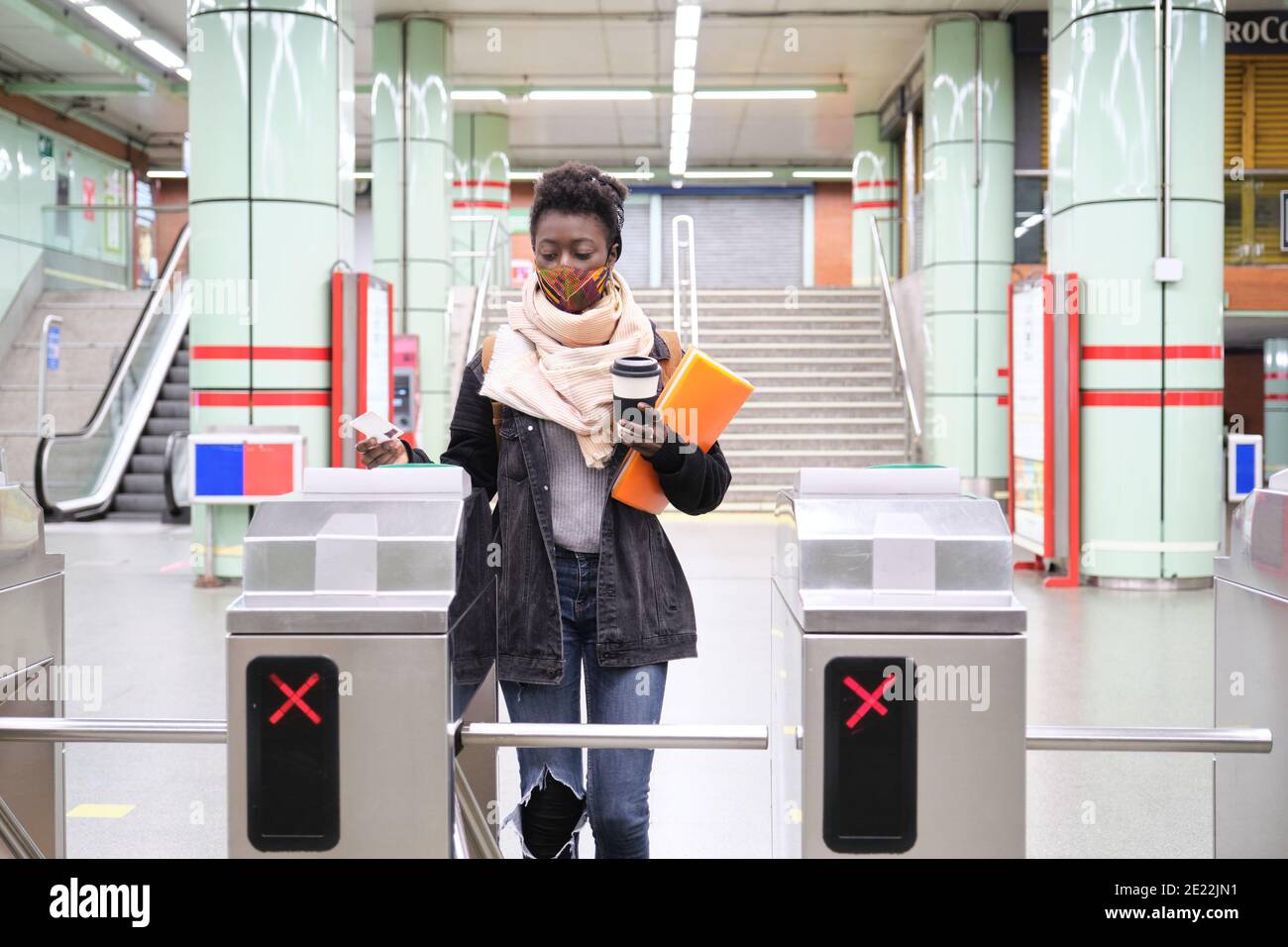 university female african student wearing protective face mask passing through the turnstiles with her transport card at the underground station. New Stock Photo