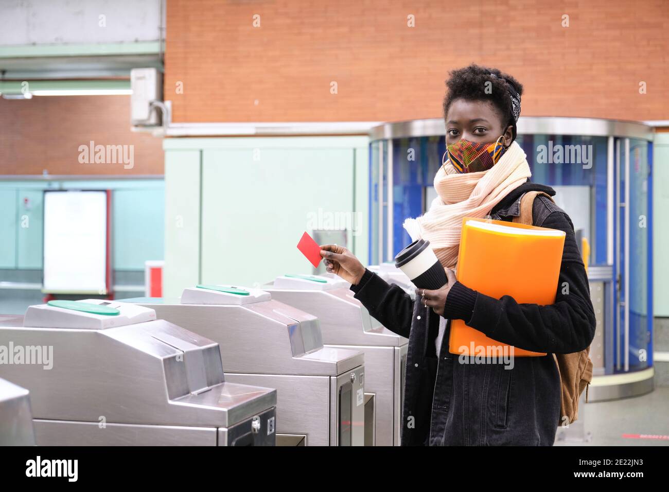 university female african student wearing protective face mask passing through the turnstiles with her transport card at the underground station. New Stock Photo