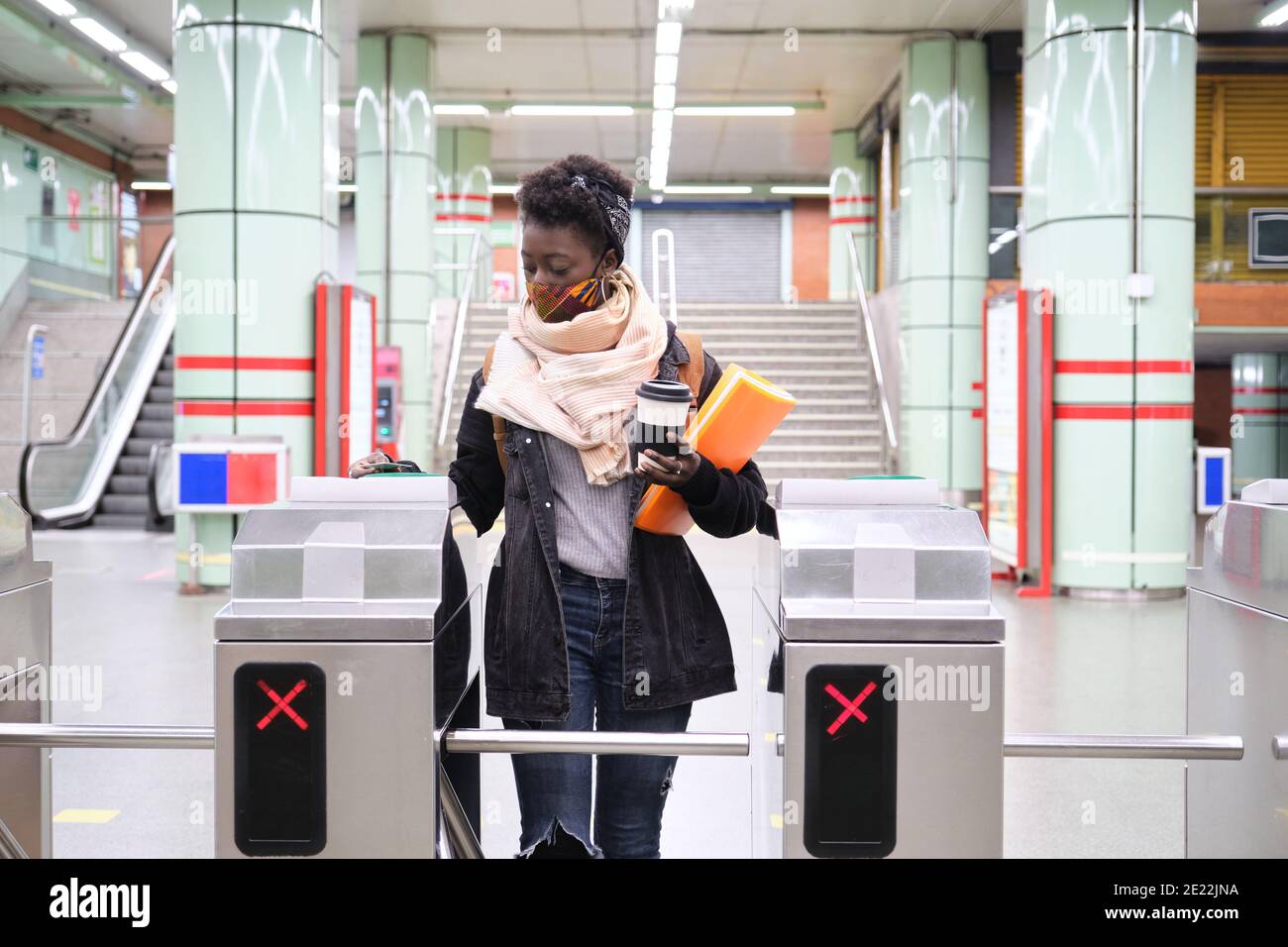 university female african student wearing protective face mask passing through the turnstiles with her transport card at the underground station. New Stock Photo