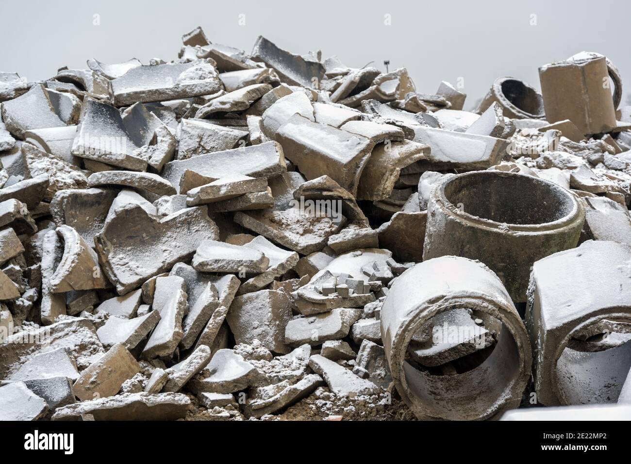 Heap of broken concrete drainage pipes under a thin layer of snow on a construction site, waiting for debris disposal, selected focus Stock Photo